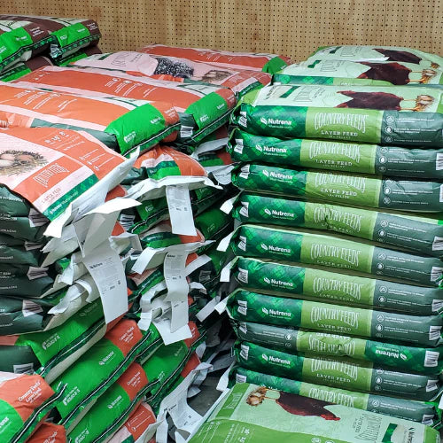 Stacks of colorful animal feed bags are neatly arranged, featuring green and orange packaging labeled 