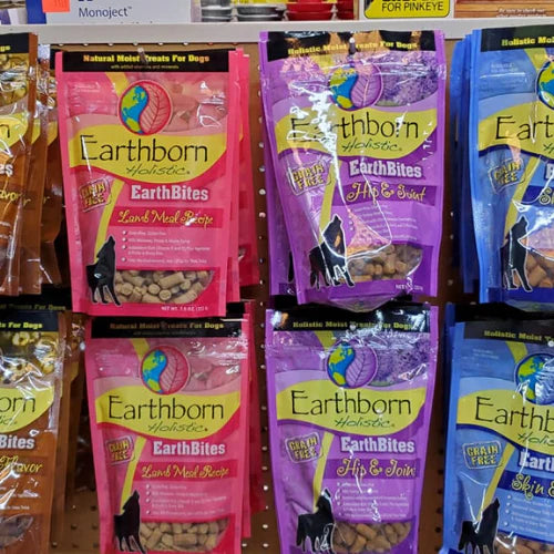 Display of various Earthborn Holistic dog treats in colorful packaging, including pink and purple bags, on a store shelf. The treats are labeled 