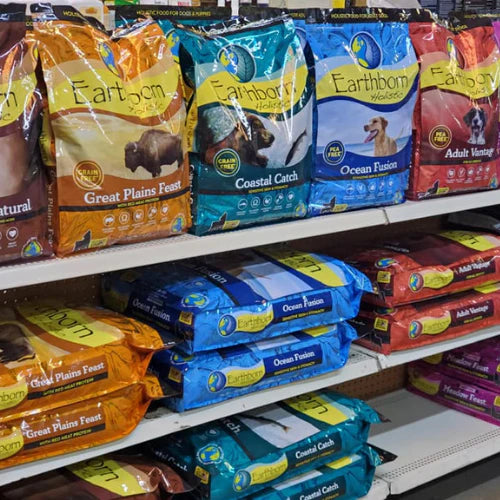 Shelves stocked with colorful bags of Earthborn Holistic dog food, featuring flavors like Coastal Catch and Great Plains Feast, in a pet store aisle.