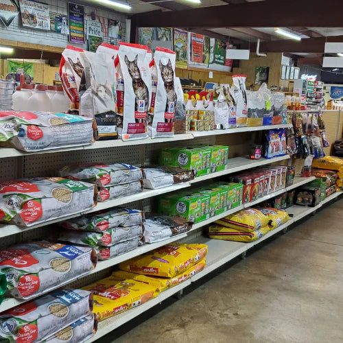 Shelves filled with various pet food brands, including cat and dog food, in a well-lit store aisle. Bright packaging creates a colorful display.