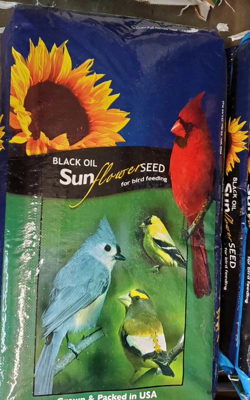 A colorful bag of black oil sunflower seeds features vibrant images of a cardinal, tufted titmouse, and goldfinches, with a sunflower backdrop.